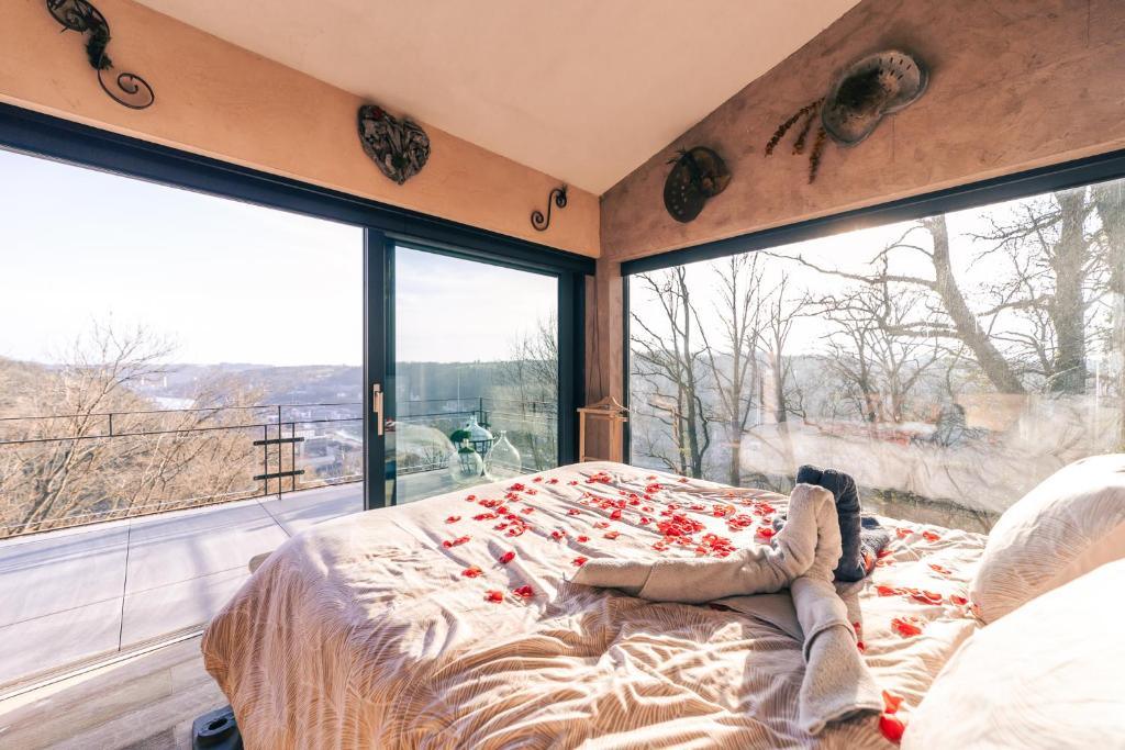 Lit king size avec pétales de roses face à une grande baie vitrée offrant une vue panoramique sur la nature et la vallée de Dinant